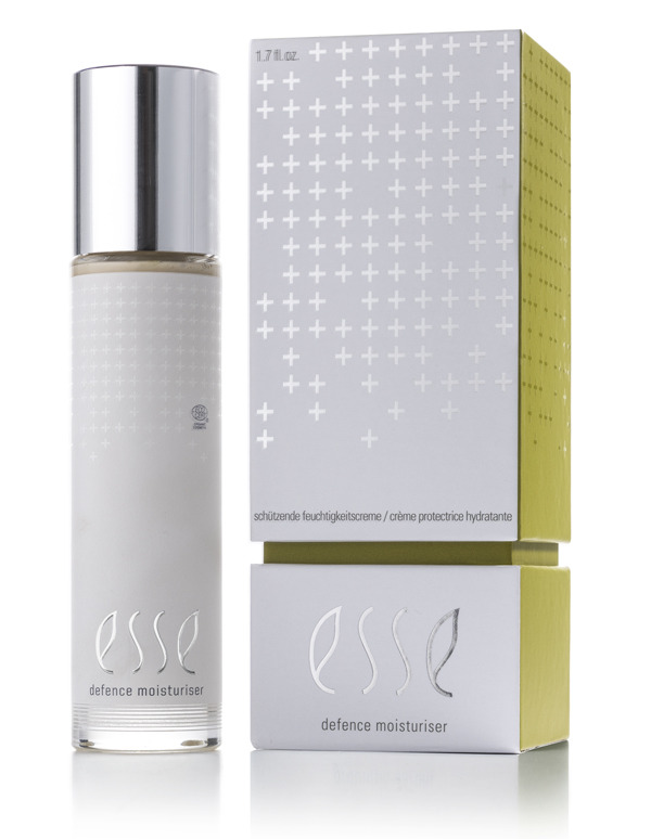 A bottle of Esse Defence Moisturiser with a silver cap is displayed next to its matching silver and yellow box, both showcasing the product name and plus-sign graphics.