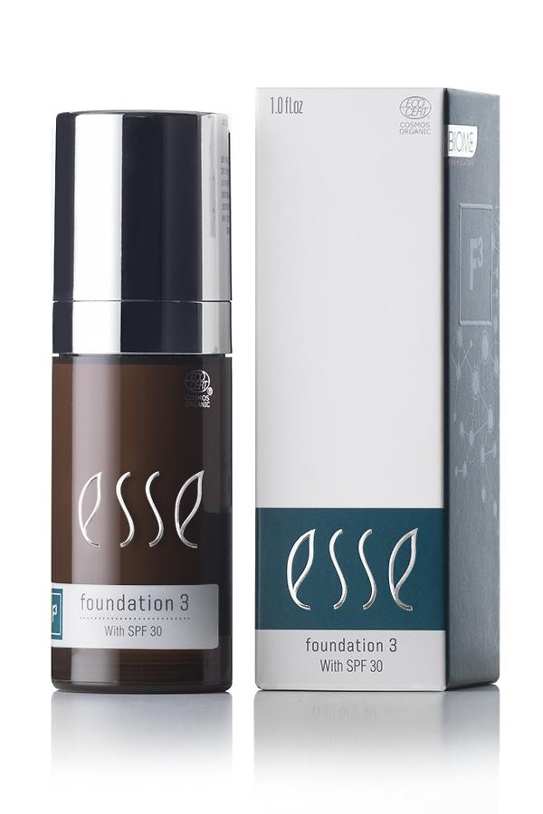A sleek pump bottle and matching box of Esse Foundation with SPF 30 are displayed side by side. The brown bottle features a silver top, while the box is white with blue accents showcasing the product name and details.