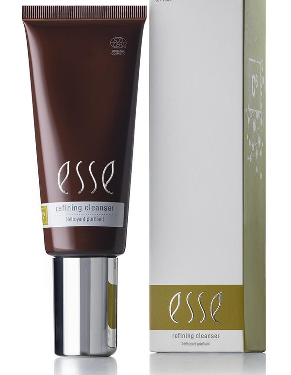 A dark brown tube and a matching box of Esse Refining Cleanser are displayed. The box is white with green accents showcasing the product label. The tube features a shiny silver cap and contains 3.4 fl oz of the Esse Refining Cleanser.