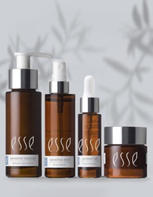 The Esse Sensitive Skin Trial/Travel Set is displayed against a light background with a faint leaf pattern, featuring a pump bottle of sensitive cleanser, a spray bottle of sensitive mist, protect oil with a dropper, and a small jar of protective cream.
