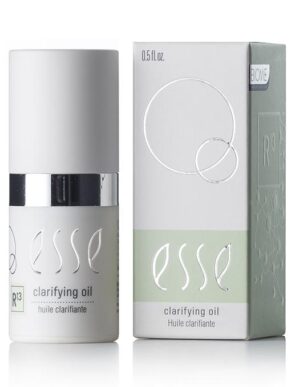The image features a bottle of Esse Clarifying Oil along with its packaging. The cylindrical bottle is adorned with a white cap and a metallic silver band. The light green and white box showcases the product name and various branding elements. The bottle has a capacity of 0.5 fl oz.