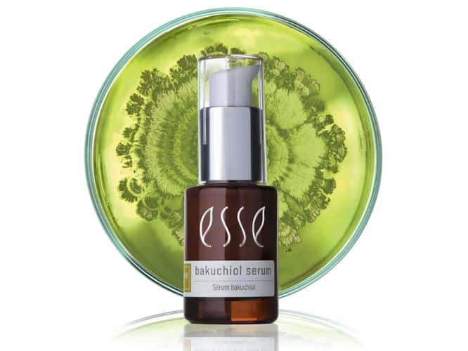 A bottle of Esse Bakuchiol Serum with a pump dispenser sits in front of a green background featuring a circular botanical design. The bottle is brown with a white label displaying the product name.