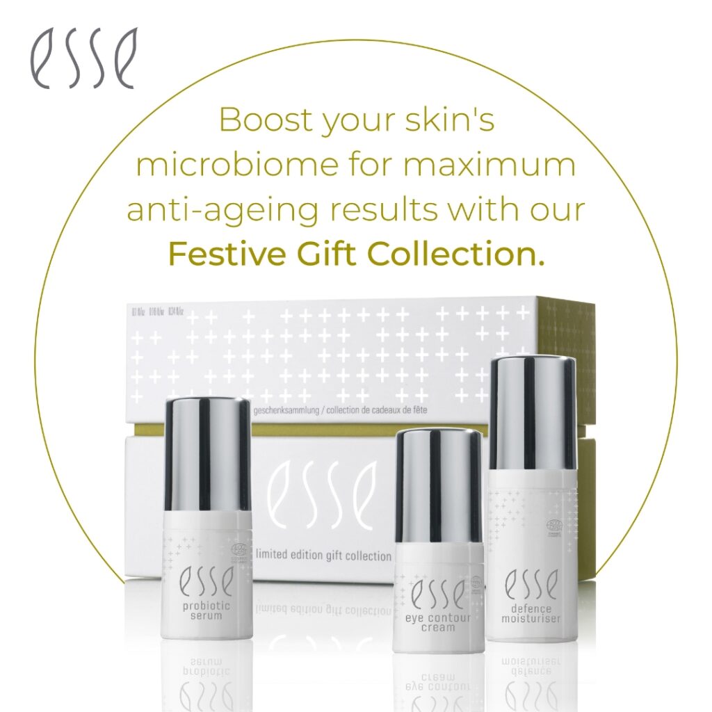 An advertisement for Esse skincare featuring their Festive Gift Collection. The image shows three bottles labeled "probiotic serum," "eye contour cream," and "defense moisturizer" in front of a sleek box set. Text above reads, "Boost your skin's microbiome for maximum anti-ageing results with our Festive Gift Collection.